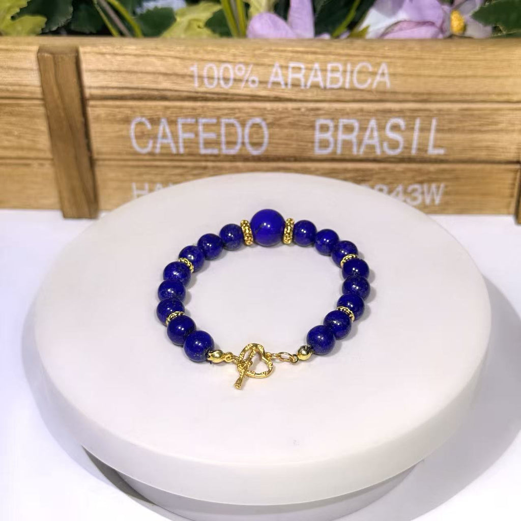 Hand-assembled natural Afghan Lapis Lazuli focal bracelet featuring a prominent 12mm centerpiece gemstone bead on a 10mm bead strand with gold accent spacers and an artisan gold heart toggle clasp.
