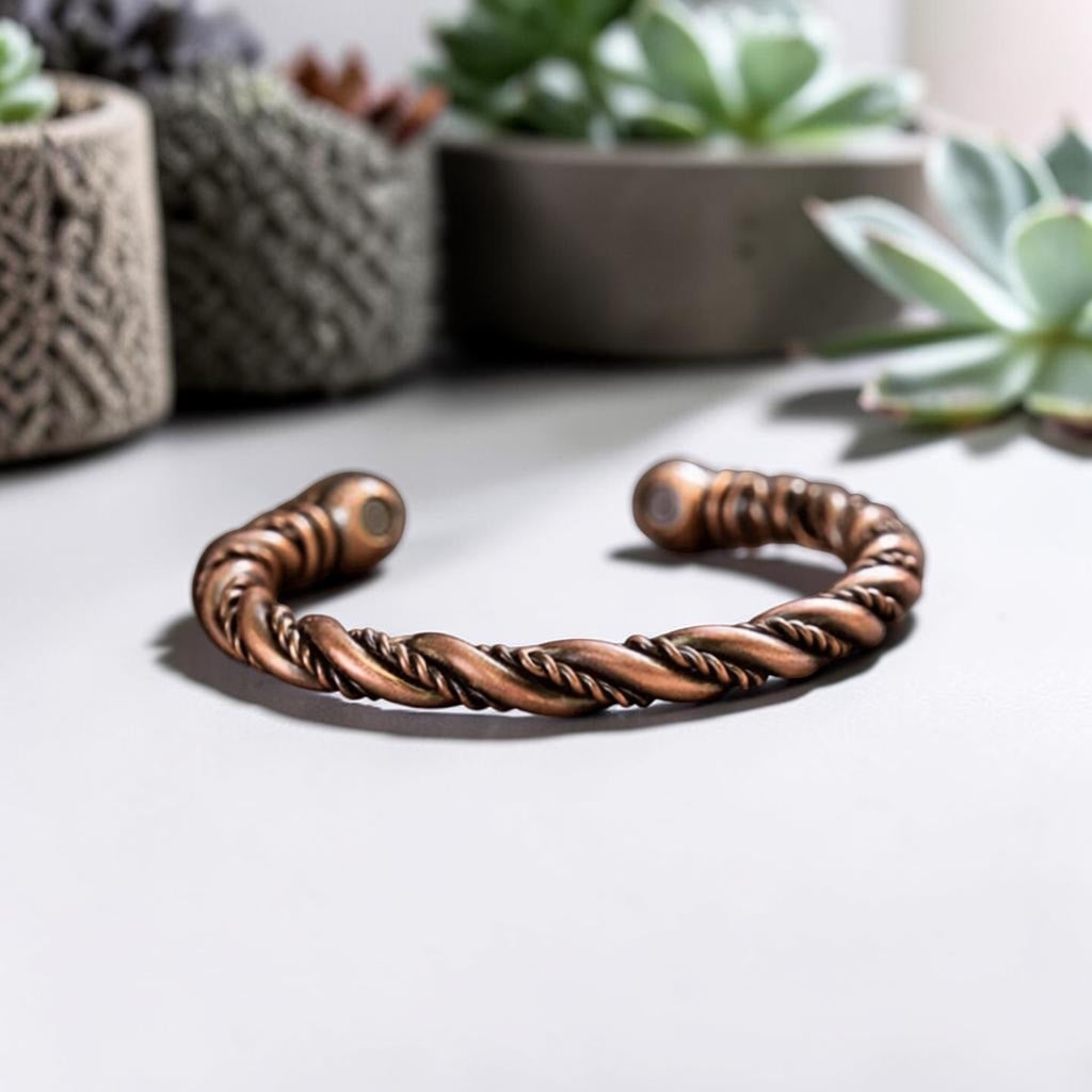 Bronze braided bracelet on a light surface with plants in the background