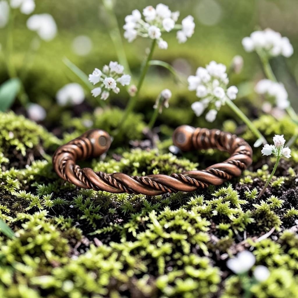 BoxUnboxed Element Cuff, a twisted pure copper magnetic bracelet resting on mossy ground with small white flowers.