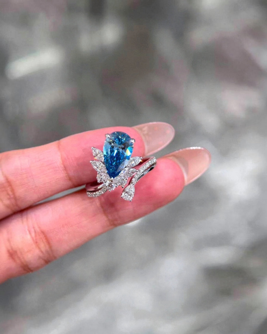 BoxUnboxed pear-cut vivid blue lab-grown diamond ring with floral-inspired diamond accents in a polished metal setting.